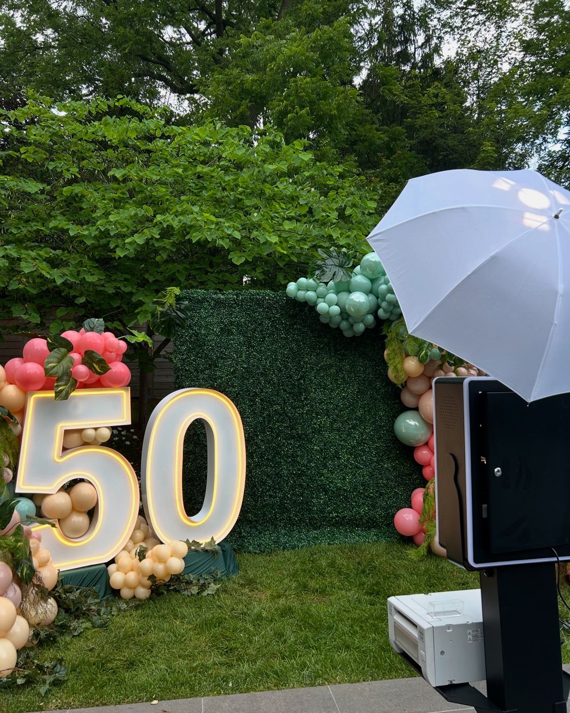 Outdoor 50th birthday photobooth setup with balloons and greenery wall