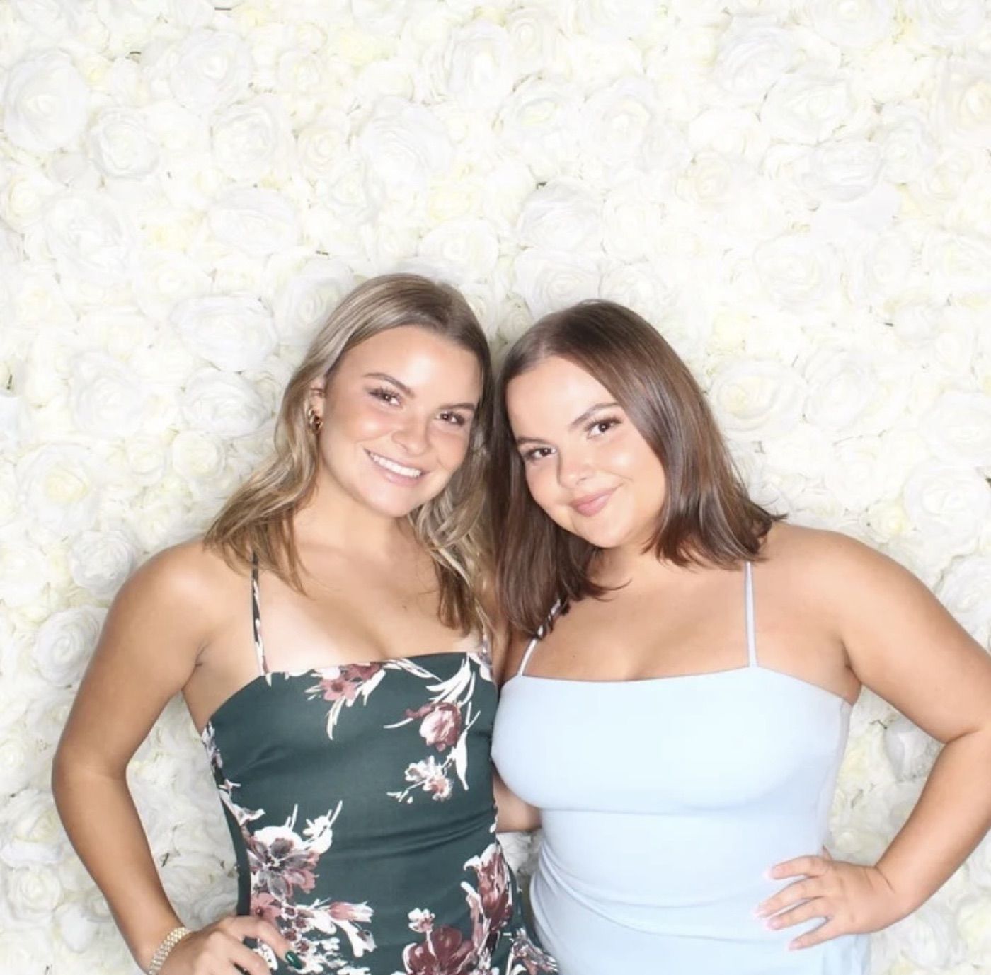 Two guests posing in front of a flower wall backdrop